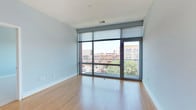 This contemporary single-floor residence combines modern design with urban living, offering a thoughtfully laid-out interior with high-quality finishes throughout. The open-concept living area is a standout feature, showcasing expansive floor-to-ceiling windows framed in dark metal that flood the space with natural light and frame sweeping views of the surrounding cityscape, including charming historic architecture. Light hardwood floors extend throughout the living and dining areas, creating a warm and inviting atmosphere.

The kitchen is seamlessly integrated into the living space and features rich, dark-stained cabinetry with sleek bar-pull hardware, granite countertops with a classic subway tile backsplash, and a full suite of stainless steel appliances, including a range, microwave, and refrigerator. A breakfast bar provides a natural transition between the kitchen and living area.

The bedroom offers plush wall-to-wall carpeting and its own window with urban views, complemented by access to a well-organized walk-in closet outfitted with wire shelving and hanging rods. The bathroom is finished with light tile flooring, a dark wood vanity with a light stone countertop, a framed mirror, and efficient built-in shelving. A secondary bathroom provides additional convenience, also featuring tile floors and a matching dark wood vanity.