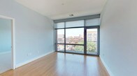 This contemporary single-floor residence combines modern design with urban living, offering a thoughtfully laid-out interior with high-quality finishes throughout. The open-concept living area is a standout feature, showcasing expansive floor-to-ceiling windows framed in dark metal that flood the space with natural light and frame sweeping views of the surrounding cityscape, including charming historic architecture. Light hardwood floors extend throughout the living and dining areas, creating a warm and inviting atmosphere.

The kitchen is seamlessly integrated into the living space and features rich, dark-stained cabinetry with sleek bar-pull hardware, granite countertops with a classic subway tile backsplash, and a full suite of stainless steel appliances, including a range, microwave, and refrigerator. A breakfast bar provides a natural transition between the kitchen and living area.

The bedroom offers plush wall-to-wall carpeting and its own window with urban views, complemented by access to a well-organized walk-in closet outfitted with wire shelving and hanging rods. The bathroom is finished with light tile flooring, a dark wood vanity with a light stone countertop, a framed mirror, and efficient built-in shelving. A secondary bathroom provides additional convenience, also featuring tile floors and a matching dark wood vanity.