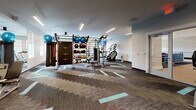Located at Patriot Lincoln Blvd in North Charleston, SC, this single-floor fitness center offers a comprehensive workout environment designed to accommodate a wide range of exercise routines. The space is organized into distinct functional zones, each thoughtfully arranged to maximize usability and flow.

The cardio area features a row of Matrix treadmills positioned along a windowed wall, where roller shades filter natural light from multiple large windows offering views of the surrounding landscaping. Mounted flat-screen televisions provide entertainment for cardio users. The open floor plan transitions into a functional training zone anchored by a multi-station rig outfitted with resistance bands, medicine balls, kettlebells, battle ropes, and TRX suspension trainers. A stair climber and additional cardio equipment are also present in this area.

The strength training section is equipped with a selection of selectorized machines and free weight benches, complemented by floor-to-ceiling mirrors that enhance the sense of openness. Linear LED lighting runs throughout the ceiling, providing consistent, bright illumination. The flooring features a patterned, multi-tone carpet tile with teal accent inlays, contributing to the modern, clean aesthetic of the overall space.