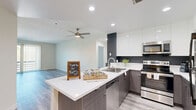 Located in the heart of Los Angeles, this well-appointed 3-bedroom, 3-bathroom residence offers a thoughtfully designed single-floor layout with modern finishes throughout. Light-toned luxury vinyl plank flooring runs seamlessly across the living spaces, complementing the clean, contemporary aesthetic.

The open-concept kitchen is a standout feature, showcasing two-tone cabinetry with dark lower cabinets and high-gloss white upper cabinets, a white quartz peninsula with a stainless steel sink, and a full suite of stainless steel appliances including a range, microwave, dishwasher, and refrigerator. Recessed lighting and a dark accent wall add depth and a modern edge to the space, which flows naturally into the living area.

The living room is generously proportioned, featuring built-in lower cabinetry with open shelving above and sliding glass doors leading to a private balcony with views of the surrounding neighborhood. A ceiling fan adds comfort to the space.

Each bedroom is bright and well-sized, with large windows fitted with vertical blinds that invite natural light. The spacious primary bedroom offers ample room for furnishings. The bathrooms are finished in clean white tile, featuring a soaking tub-shower combination with brushed gold fixtures and a floating vanity with white countertop. Four closets and a dedicated utility room provide excellent storage throughout.