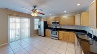 This multi-floor residence is thoughtfully laid out across three levels, offering a range of functional spaces with consistent neutral tones and warm beige walls throughout. The kitchen is a standout area, featuring light maple cabinetry, dark granite countertops, tile flooring, and a full suite of stainless steel appliances including a refrigerator with ice maker, electric range, and over-the-range microwave. A ceiling fan and sliding glass door with vertical blinds bring natural light and ventilation into the kitchen area. The carpeted living and bedroom spaces are generously sized, each equipped with ceiling fans and large windows that invite natural light. Multiple rooms feature sliding glass doors that open directly onto an outdoor deck with white railings, offering pleasant outdoor views. A full bathroom includes tile flooring, a white vanity with storage, a combined tub and shower unit, recessed lighting, and a large mirror. A dedicated laundry area provides wire shelving, a closet with bi-fold doors, and hookups for a washer and dryer. The attached garage features a concrete floor and an automatic garage door opener, providing secure and convenient vehicle storage. Overall, the property presents a clean, practical layout suited for comfortable everyday living.
