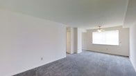 This single-floor space offers a straightforward, functional layout designed for comfortable everyday living. The open living area is finished with plush grey carpeting that extends throughout, creating a cohesive and understated aesthetic. Bright white walls provide a neutral backdrop that enhances the sense of openness, while smooth ceilings contribute to the clean, uncluttered feel of the interior.

A ceiling fan is centrally positioned in the living area, offering both light and air circulation, and a large window invites an abundance of natural light, brightening the space throughout the day. The layout includes a built-in closet with bifold doors, providing convenient and organized storage within the main living area.

The overall ambiance is calm and minimal, with a palette of whites and soft greys that lends itself well to a variety of furnishing styles. The space is move-in ready, offering a blank canvas that allows residents to personalize and arrange to their preferences. The straightforward floor plan ensures easy navigation and flow between areas, making it a practical and welcoming environment for daily living.