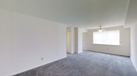 This single-floor space offers a straightforward, functional layout designed for comfortable everyday living. The open living area is finished with plush grey carpeting that extends throughout, creating a cohesive and understated aesthetic. Bright white walls provide a neutral backdrop that enhances the sense of openness, while smooth ceilings contribute to the clean, uncluttered feel of the interior.

A ceiling fan is centrally positioned in the living area, offering both light and air circulation, and a large window invites an abundance of natural light, brightening the space throughout the day. The layout includes a built-in closet with bifold doors, providing convenient and organized storage within the main living area.

The overall ambiance is calm and minimal, with a palette of whites and soft greys that lends itself well to a variety of furnishing styles. The space is move-in ready, offering a blank canvas that allows residents to personalize and arrange to their preferences. The straightforward floor plan ensures easy navigation and flow between areas, making it a practical and welcoming environment for daily living.