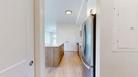 Located at 7219 Sharon Ave in Niagara Falls, Ontario, this well-appointed one-bedroom, two-bathroom unit offers a thoughtfully designed layout with modern finishes throughout. Light hardwood flooring flows seamlessly across the entire living space, complementing the neutral, soft-toned walls and creating a bright, cohesive aesthetic.

The open-concept kitchen is a standout feature, equipped with stainless steel appliances including a range, microwave, dishwasher, and refrigerator. Warm wood-toned lower cabinetry is paired with crisp white upper cabinets, finished with matte black hardware. A classic white subway tile backsplash adds texture, while the spacious central island with a white quartz countertop provides additional prep and dining space.

The living area is generously proportioned, with large windows inviting abundant natural light and offering pleasant views of the surrounding greenery. The bedroom continues the bright theme, featuring a large window with outdoor views, a double-door closet, and warm hardwood flooring.

Both bathrooms are finished to a high standard. One features a floating wood-toned vanity with a white quartz countertop and large-format tile flooring, while the other includes a glass-enclosed shower with clean white horizontal tile. The unit also includes an in-suite laundry area, adding everyday convenience to this refined and modern space.