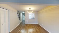 This two-story residence in Indianapolis, IN offers a well-organized layout across two distinct floors. The main level opens into a spacious living area finished with warm hardwood-style flooring that extends throughout. A striking multi-ring circular chandelier serves as a focal point, casting layered ambient light across the open space. A pass-through window connects the living area to the kitchen, maintaining an open, communicative flow between rooms. The kitchen is thoughtfully appointed with white cabinetry featuring matte black hardware, dark granite-style countertops, a white subway tile backsplash, a stainless steel sink with a black faucet, and black appliances including an electric range. A louvered closet door and staircase with black metal railings are also found on the main level, along with convenient floor vents throughout.

The upper level features carpeted bedrooms finished in neutral tones, providing a quieter, comfortable setting. One bedroom benefits from a window with outdoor views, allowing natural light to fill the space. The bathroom on this level includes a white vanity with a speckled countertop, undermount sink, a large mirror, matte black fixtures, and a shower with a curtain rod, all presented in a clean, updated style.