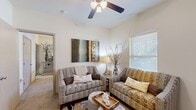 This efficiently designed single-story unit offers a thoughtful layout across its four distinct spaces. The combined kitchen and living area serves as the heart of the unit, where the kitchen features rich dark wood cabinetry, granite-style countertops, black appliances, and a breakfast bar with seating — all complemented by wood-look flooring and a ceiling fan overhead. The open living area flows naturally from the kitchen, showcasing plush carpeting, a ceiling fan with light fixture, and a bright window with blinds that invites natural light into the warm, neutral-toned space.

The primary bedroom is a cozy retreat finished with soft carpeting, a ceiling fan, and a window that frames views of the surrounding greenery. The bathroom features dark wood vanity cabinetry, a white countertop with sink, a framed mirror, and wood-look flooring, offering a clean and functional aesthetic. A dedicated laundry area provides in-unit convenience, complete with a top-load washer, wire shelving for storage, and a water heater tucked neatly alongside. Throughout the unit, neutral wall tones and consistent finishes create a cohesive and welcoming ambiance.