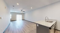 Located at 115 SW Eagles Pkwy in Grain Valley, Missouri, this single-floor unit offers a thoughtfully designed open-concept layout that seamlessly connects the main living areas. Light wood-style flooring flows throughout the common spaces, complemented by recessed lighting and ceiling fans that enhance both comfort and visual appeal.

The kitchen serves as a functional centerpiece, featuring a bold navy-blue island with granite countertops and an integrated stainless steel sink. Gray shaker-style cabinetry lines the walls alongside a classic subway tile backsplash, while stainless steel appliances—including a refrigerator, range, and built-in microwave—complete the well-appointed space. The island opens naturally toward the living area, which benefits from a sliding glass door that invites natural light and provides outdoor access.

The bedrooms are finished with plush carpeting and ceiling fans, offering a comfortable contrast to the hard-surface common areas. Each bedroom includes access to a walk-in closet, providing generous storage. The bathroom is outfitted with granite-topped vanity and a full tub-shower combination, maintaining the consistent modern aesthetic found throughout the unit. Dark-finished interior doors add a sharp, contemporary accent across all rooms.
