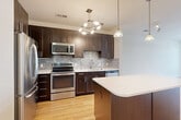 Located at 2677 Avenir Pl in Vienna, VA, this well-appointed 1-bedroom, 1-bathroom residence offers a thoughtfully designed single-floor layout that maximizes every square foot. The open-concept living and dining area is bright and airy, featuring warm hardwood flooring and a sliding glass door that opens to a private balcony, allowing natural light to flow in through a transom window above. The modern kitchen is a standout feature, showcasing rich dark-espresso cabinetry, a mosaic tile backsplash, light quartz countertops, and a full suite of stainless steel appliances including a refrigerator, range, microwave, and dishwasher. A center island with matching cabinetry provides additional prep space and casual seating, illuminated by contemporary pendant lighting. The bedroom is comfortably sized, finished with plush carpet and a window overlooking the exterior. The bathroom offers a clean, contemporary design with dark wood vanity cabinetry, white countertops, large-format tile flooring, and a tub-shower combination. Additional spaces include a den, dedicated laundry area, entrance foyer, hallway, and two closets, offering practical storage and versatile use throughout the home.