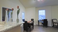 This single-floor residence offers a thoughtfully designed open-concept layout that seamlessly connects the main living areas, creating a sense of spaciousness and flow. The dining area is a standout feature, showcasing impressively vaulted ceilings that draw the eye upward and amplify the room's airy feel. Natural light pours in through multiple large windows dressed with horizontal blinds, brightening the neutral-toned walls and enhancing the overall warmth of the space. The dining area comfortably accommodates a round dining table with dark upholstered chairs, making it well-suited for both casual meals and entertaining. An adjacent countertop with a striking granite surface — featuring light tones and subtle veining — hints at a well-appointed kitchen nearby. Durable wood-look flooring runs throughout, offering both aesthetic appeal and practical functionality. A glass-paneled door provides convenient access to the exterior, further enhancing the connection to the outdoors and allowing additional natural light into the space. Track lighting overhead adds a modern touch and ensures the room is well-lit at any hour. The overall ambiance is clean, contemporary, and inviting, with a neutral palette that provides a versatile backdrop for a variety of interior styles.