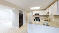 This single-floor residence in Jacksonville, FL (32205) offers a clean, functional layout with consistent light tile flooring and neutral gray walls throughout. The kitchen is a clear highlight, showcasing crisp white shaker-style cabinetry, granite countertops, and a matching peninsula that provides additional prep space and casual seating. Black appliances — including a range with over-the-range microwave, refrigerator, and dishwasher — complement the bright cabinetry, while a double stainless steel sink adds practicality. A louvered bifold door nearby offers access to a utility or storage closet. The living area is spacious and open, featuring large tile flooring and a sliding glass door that invites natural light and connects to the outdoors. The additional room is generously sized with the same tile flooring, offering flexibility as a bedroom or multi-use space. Two bathrooms serve the home: one features a tub-shower combination with white tile surround, while the other includes a granite vanity top, a mirrored medicine cabinet, and a curtained shower. Textured ceilings are present throughout, adding subtle architectural character. Overall, the space presents a cohesive, move-in ready environment with practical finishes and a light, airy atmosphere.