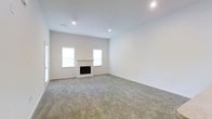This single-floor space offers a clean, modern design defined by bright, open interiors and a neutral color palette. The main living area is immediately impressive, boasting soaring vaulted ceilings that amplify the sense of spaciousness and airiness throughout the room. Recessed lighting is strategically placed across the ceiling, supplementing the abundant natural light that pours in through multiple windows flanking a sleek, built-in fireplace — a standout focal point of the living space. The fireplace features a minimalist white surround that blends seamlessly with the crisp white walls, contributing to the space's contemporary aesthetic. Plush, neutral-toned carpeting covers the floors, adding warmth and comfort underfoot while complementing the understated, versatile design. A ceiling fan is also present, ensuring year-round comfort. The overall ambiance is calm, airy, and move-in ready, with a fresh, uncluttered environment that provides an excellent canvas for a variety of interior styles. The thoughtful layout and high-quality finishes make this a well-appointed and inviting space.
