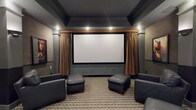 Located at 5199 Edwards Farms Rd in Hilliard, Ohio, this single-floor space is highlighted by a thoughtfully designed home theater room that delivers an immersive cinematic experience. The theater is anchored by a large, centrally mounted projection screen framed by floor-to-ceiling golden drape panels, lending a classic movie-house aesthetic to the room. A custom valance above the screen adds an architectural finishing touch, while built-in recessed speakers flanking the screen ensure high-quality audio performance.

The ceiling features a tray-style design finished in deep charcoal tones, contributing to the room's light-controlled, theater-like atmosphere. Recessed lighting is strategically placed to provide ambient illumination without detracting from the viewing experience. The flooring is covered in a neutral checkered carpet that adds texture and visual interest underfoot while also aiding in sound absorption.

Seating consists of dark leather chairs paired with matching leather ottomans, arranged to optimize sightlines to the screen. The overall color palette — combining slate gray walls, dark ceiling tones, and warm gold drapery accents — creates a sophisticated, intimate ambiance well-suited for private screenings and entertainment.