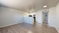 This efficient and thoughtfully designed single-level residence offers a comfortable layout across 1 bedroom and 1 bathroom. The open-concept living and kitchen area serves as the heart of the unit, featuring rich wood-look laminate flooring and a light gray color palette that lends the space a clean, modern feel. A peninsula-style breakfast bar separates the kitchen from the living area, providing both a functional prep surface and a casual dining option. The kitchen is well-equipped with white cabinetry, light stone-look countertops, a classic white subway tile backsplash, and stainless steel appliances including a microwave and range, complemented by a black refrigerator. The living area benefits from a window that allows natural light to fill the space. The bedroom offers plush carpeting, a ceiling fan, and a window with blinds for added comfort and privacy. A dedicated closet provides practical storage. The full bathroom features wood-look flooring, a full tub-shower combination, and clean white finishes throughout. The entry area, also finished with wood-look flooring, completes this cohesive and efficiently planned residence.