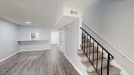 Located at 1655 20th Avenue Dr NE in Hickory, NC, this two-story home offers three bedrooms and two bathrooms across two well-organized floors. The main level provides the more expansive living footprint, featuring durable wood-look LVP flooring, neutral gray walls, and a textured ceiling throughout. A staircase with a sleek black metal railing connects the two levels, while a pass-through window area hints at a functional kitchen layout. The main living area is bright and open, highlighted by a sliding glass door that invites natural light and outdoor views. A standout bedroom on the main floor features distinctive shiplap wall paneling, adding a modern farmhouse character to the space. The upper floor houses the remaining bedrooms, including the primary bedroom, which is carpeted and features a louvered bi-fold closet for ample storage. Additional bedrooms on this level are also carpeted, each with windows that bring in natural light and views of surrounding greenery. A hallway connects the upper-level rooms with convenient access to shared spaces. The bathrooms are clean and functional, featuring a full tub-shower unit. Throughout the home, consistent neutral tones, white trim, and updated fixtures create a cohesive, move-in-ready aesthetic.