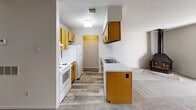 Located at 2707 S Emporia St in Wichita, Kansas, this single-floor, one-bedroom, one-bathroom unit offers a functional and straightforward layout. The kitchen is well-equipped with warm honey-toned wood cabinetry, a white electric range, refrigerator, dishwasher, and a peninsula with a built-in sink and additional counter space. Wood-look flooring runs through the kitchen area, transitioning into plush carpet throughout the rest of the unit. The open living area receives natural light through a large sliding glass door fitted with vertical blinds, and features a distinctive corner fireplace that serves as a focal point of the room. Textured ceilings are present throughout the unit, lending a classic residential character. The bedroom is a comfortable, carpet-floored room with a window for natural light and two side-by-side closets offering generous storage space. The unit's neutral color palette of whites and soft grays creates a clean, move-in-ready feel. Overall, the layout is efficient and well-organized, making practical use of every square foot available.