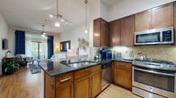Located along the Katy Freeway corridor in Houston, TX, this one-bedroom, one-bathroom residence offers a thoughtfully designed single-floor layout that maximizes comfort and functionality. The open-concept living and dining area is anchored by warm hardwood flooring, a ceiling fan, and a sliding glass door that draws in natural light and provides access to an outdoor balcony. The kitchen is a standout feature, boasting rich dark wood cabinetry, dark granite countertops, a mosaic tile backsplash, stainless steel appliances including a gas range, microwave, dishwasher, and refrigerator, and pendant lighting above a peninsula with bar seating — ideal for casual dining or entertaining. The bedroom is a serene retreat featuring plush carpeting, a ceiling fan, generous natural light from large windows with blinds, and two closets, including a walk-in closet with wire shelving. The bathroom is finished with slate tile flooring, a granite vanity, and a glass-enclosed walk-in shower. An in-unit washer and dryer area adds everyday convenience. Throughout the residence, elevated ceilings and a bright, neutral palette create a spacious and inviting atmosphere.