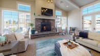This single-story community clubhouse is designed to provide a refined and comfortable gathering space for residents. The entrance greets visitors with soaring double-height ceilings, large transom windows that flood the foyer with natural light, and elegant tile flooring accented by a decorative patterned area rug. A teal console cabinet and framed artwork add a curated, welcoming touch near the entry.

A wide corridor with wainscoting, tile flooring, and tasteful décor—including a tufted bench and potted plants—connects the entry to the main living areas. Glass sliding doors offer a seamless visual connection between spaces, enhancing the open flow throughout.

The main lounge is a standout feature, anchored by a dramatic stacked-stone fireplace with a raised hearth and mounted flat-screen television above. Vaulted ceilings with exposed beams and an abundance of large windows provide sweeping outdoor views and excellent natural light. Comfortable seating arrangements make the space ideal for both relaxed gatherings and social events.

An adjacent kitchen area features rich dark wood cabinetry, light granite countertops, stone tile backsplash, stainless steel appliances, and a coffee station, offering full amenities for resident use. Tile flooring runs throughout the kitchen, maintaining a cohesive, polished aesthetic across the entire facility.