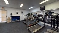 This single-floor fitness center offers a comprehensive workout environment designed to accommodate a wide range of exercise routines. The cardio area is outfitted with multiple treadmills from Vision Fitness and Star Trac, as well as a stair climber, all arranged in a row and complemented by wall-mounted flat-screen televisions for entertainment during workouts. Large mirrors line the walls, enhancing the sense of space and allowing users to monitor their form throughout their sessions. Fluorescent ceiling lighting ensures the entire facility is well illuminated.

The strength and functional training zone features a dumbbell rack with a variety of weights, an adjustable workout bench, and a multi-station cable machine. A dedicated wall-mounted medicine ball rack provides options for dynamic and functional exercises. A recumbent stationary bike offers a low-impact cardio alternative, while additional cable and pulley attachments support upper-body training.

Throughout the space, University of Arizona Wildcats signage and logos reinforce a spirited athletic atmosphere. Dark commercial-grade carpet covers the floor, providing durability underfoot. A standing fan and a wall-mounted sanitation dispenser reflect attention to user comfort and hygiene. The open layout and diverse equipment selection make this fitness center suitable for both cardio-focused and strength-training workout regimens.