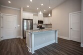 Located at 300 S Tulane Ave in Oak Ridge, Tennessee, this well-appointed single-floor residence offers a thoughtfully designed open-concept layout with modern finishes throughout. The kitchen serves as a central highlight, featuring white shaker cabinetry, granite-style countertops, a tile backsplash, and a full suite of stainless steel appliances including a refrigerator, range, microwave, and dishwasher. A kitchen island with an undermount sink and elegant pendant lighting adds both functionality and visual appeal, while soaring vaulted ceilings create an impressive sense of openness as the space flows into the living area. The living room is bright and airy, benefiting from natural light through large windows and a ceiling fan overhead. Wood-look flooring runs throughout the main living areas, while the bedrooms feature plush carpeting for added comfort. Each bedroom is generously sized with ceiling fans and natural light. The primary bathroom is equipped with a granite-topped vanity, wood-look flooring, and access to a walk-in closet. A secondary full bathroom includes a tub/shower combination, a single vanity with granite countertop, and wood-look flooring. The unit also includes a dedicated pantry closet, providing ample storage. The overall ambiance is clean, contemporary, and move-in ready.