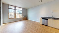 This thoughtfully designed single-floor unit offers a clean, contemporary aesthetic throughout. The open-plan living area is bathed in natural light through large windows that frame striking urban city views, with warm hardwood flooring and track lighting adding to the bright, airy ambiance.

The kitchen is efficiently laid out in an L-shaped configuration, featuring light maple cabinetry, dark countertops, and a full suite of stainless steel appliances including an electric range, over-the-range microwave, and dishwasher. Ample upper and lower cabinet storage makes this kitchen as functional as it is stylish.

The bedroom is generously proportioned with notably high ceilings that enhance the sense of space. A sliding door opens to a well-organized walk-in closet with built-in shelving and hanging storage, providing excellent organizational capacity.

The bathroom is finished to a consistent standard, featuring a light maple vanity with dark countertop, an undermount sink, a large mirror with overhead lighting, and a full bathtub with shower. Hardwood flooring carries through from the main living areas, tying the space together cohesively.

Overall, the unit presents a modern, neutral palette with clean lines and quality finishes, creating a comfortable and functional living environment.