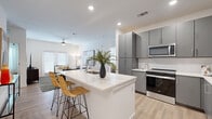 This single-floor residence offers a well-designed, open-concept layout with a clean, contemporary aesthetic carried consistently throughout. Light wood-look flooring runs through the main living areas, complementing the bright white walls and recessed lighting that give the space an airy, modern feel.

The kitchen serves as a central hub, anchored by a large island with a quartz countertop, an integrated sink, and bar seating. Gray flat-front cabinetry extends to the ceiling for ample storage, while stainless steel appliances — including a refrigerator with ice maker, range, microwave, and dishwasher — provide a polished, functional finish. A white subway tile backsplash adds a subtle classic detail.

The living area is generously sized and benefits from natural light through sliding glass doors and large windows fitted with blinds. A ceiling fan adds comfort to the open space.

The two bedrooms are well-proportioned, each featuring ceiling fans or lighting fixtures and windows allowing natural light. One bedroom includes a distinctive accent wall, while the other offers a bright, neutral palette. A walk-in closet with wire shelving provides practical storage.

The bathroom is clean and minimal, featuring a gray floating vanity with a white countertop, a large mirror, and a full soaking tub with a shower curtain. A hallway with built-in storage connects the living and private areas of the residence.