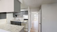 Located at 1048 Cross Keys Rd in Lexington, Kentucky, this single-floor unit offers a well-organized and functional layout throughout. The galley-style kitchen is a standout feature, outfitted with gray cabinetry, granite-style countertops, a double stainless steel sink, and a full suite of appliances including a refrigerator, electric range, and vent hood. Wood-look luxury vinyl plank flooring runs throughout the space, providing a cohesive and easy-to-maintain surface. The living area is bright and open, benefiting from a large picture window that allows generous natural light to fill the room, along with a sliding glass door that opens directly onto a private balcony with outdoor views. Ceiling fans are installed in both the living area and additional rooms, ensuring comfortable airflow. The bedrooms are comfortably sized, each featuring neutral gray walls, ceiling fans, and closets with built-in shelving for organized storage. The bathroom retains classic retro character with warm yellow wall tiling accented by gray lower cabinetry and a tub-shower combination. Textured ceilings are found throughout, adding a traditional architectural detail. The overall ambiance is clean, neutral, and move-in ready, with updated finishes that complement the home's practical and comfortable design.