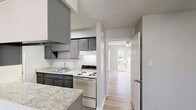 Located at 1048 Cross Keys Rd in Lexington, Kentucky, this single-floor unit offers a well-organized and functional layout throughout. The galley-style kitchen is a standout feature, outfitted with gray cabinetry, granite-style countertops, a double stainless steel sink, and a full suite of appliances including a refrigerator, electric range, and vent hood. Wood-look luxury vinyl plank flooring runs throughout the space, providing a cohesive and easy-to-maintain surface. The living area is bright and open, benefiting from a large picture window that allows generous natural light to fill the room, along with a sliding glass door that opens directly onto a private balcony with outdoor views. Ceiling fans are installed in both the living area and additional rooms, ensuring comfortable airflow. The bedrooms are comfortably sized, each featuring neutral gray walls, ceiling fans, and closets with built-in shelving for organized storage. The bathroom retains classic retro character with warm yellow wall tiling accented by gray lower cabinetry and a tub-shower combination. Textured ceilings are found throughout, adding a traditional architectural detail. The overall ambiance is clean, neutral, and move-in ready, with updated finishes that complement the home's practical and comfortable design.