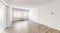 Located at 825 New Hampshire Ave NW in Washington, DC's Foggy Bottom neighborhood, Unit 205 is a thoughtfully laid-out studio offering a living area, kitchen, and full bathroom across a single floor. The living area features light-toned hardwood-style flooring and crisp white walls that create a clean, bright atmosphere. A wide window fitted with horizontal blinds allows natural light to filter in while offering views of the surrounding urban streetscape, with a radiator unit positioned beneath providing in-unit heating. The space includes a closet and entry door, contributing to practical everyday functionality. The kitchen is efficiently designed with white cabinetry, a gas range, a full-size refrigerator, a sink, and light tile flooring — maximizing utility within a compact footprint. The bathroom features classic white subway tile wainscoting along the walls, a toilet, and a vanity with a mirrored medicine cabinet, lending a timeless, clean aesthetic. Throughout the unit, the neutral color palette and consistent use of light materials contribute to an open, airy feel. The overall layout is compact yet functional, well-suited for urban living in one of Washington, DC's most walkable and centrally connected neighborhoods.
