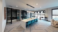 The REVA Rahway Business Center is a thoughtfully designed single-floor professional workspace located in Rahway, New Jersey. The space blends contemporary aesthetics with functional versatility, making it well-suited for collaboration, focused work, and meetings alike.

The main area centers around a striking marble-topped communal table flanked by vibrant teal chairs and illuminated by a dramatic linear pendant light fixture with cascading bulbs. Herringbone-patterned carpet throughout adds a refined textural element to the open floor plan. Adjacent to the central table, a high bar-height counter along the window wall offers additional seating and views of the surrounding area.

A cozy lounge zone features patterned swivel chairs and built-in banquette seating set against a bold geometric wood-panel accent wall, creating an intimate nook for informal gatherings or relaxed work sessions. Large floor-to-ceiling windows with roller shades flood this area with natural light and provide outdoor views.

Glass-fronted private offices or conference rooms, framed in sleek black metal, offer enclosed spaces for focused work or private meetings. Decorative open shelving with warm wood tones provides display and storage space, while curated artwork and sculptural accents contribute to the space's creative, modern character. A professional-grade printer station rounds out the practical amenities of this well-appointed business center.