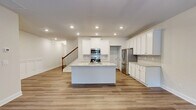 Located at 901 Porchlight Drive in Loganville, GA, this two-story home offers four bedrooms and four bathrooms spread across two well-proportioned floors. The main level features an open-concept kitchen and living area anchored by a central island with granite countertops, white shaker cabinetry, stainless steel appliances, and light hardwood-style flooring. Recessed lighting throughout adds a clean, modern feel. French doors in the living area invite natural light and provide outdoor access. The upper floor hosts the primary bedroom suite, which includes a spacious en-suite bathroom with a double vanity featuring granite countertops, a walk-in glass shower, and a private water closet. The upper hallway is distinguished by elegant wainscoting paneling and continued hardwood-style flooring. Additional bedrooms are carpeted and well-lit with natural light from double windows offering pleasant outdoor views. The home includes three closets and two hallways for ample storage and circulation. A staircase with a rich wood banister connects both levels, adding a traditional design element to the otherwise clean, contemporary aesthetic throughout the home.