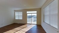 This well-appointed multi-floor property spans three levels, offering generous living space designed for comfort and functionality. The interior is characterized by warm hardwood flooring that flows throughout, complementing the neutral, light-toned walls that create a clean and inviting atmosphere.

Natural light is a defining feature of the main living area, which benefits from multiple large windows fitted with horizontal blinds, as well as a set of sliding glass doors that open onto an outdoor deck or balcony. The deck, framed by a white railing, provides pleasant views of the surrounding neighborhood, adding a sense of openness to the interior.

The living area is generously proportioned, with smooth ceilings and recessed lighting that enhance the bright, airy feel of the space. The layout is open and versatile, easily accommodating a variety of furniture arrangements to suit different lifestyle needs.

Across its three floors, this property offers a layered living experience, with ample room for dedicated spaces for rest, work, and entertainment. The combination of quality finishes, thoughtful design, and abundant natural light make this a welcoming and practical home well-suited for everyday living.
