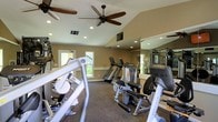 This single-floor fitness center offers a comprehensive workout environment designed to accommodate a range of exercise needs. The space features vaulted ceilings that lend an open, airy feel, complemented by recessed lighting and large ceiling fans that promote airflow and comfort during workouts. Warm-toned walls and carpeted flooring create a welcoming atmosphere throughout. The facility is outfitted with a diverse selection of equipment, including treadmills, a recumbent bike, and a variety of strength training machines from reputable brands such as Hoist and Matrix. Floor-to-ceiling mirrors line one wall, visually expanding the space and allowing users to monitor their form during exercise. Natural light filters in through windows along the perimeter, providing a bright and energizing environment. The thoughtful layout ensures adequate spacing between machines, allowing for comfortable and safe movement throughout the facility. Overall, this fitness center strikes a balance between functionality and comfort, making it a practical and inviting space for daily exercise.