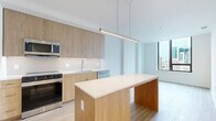 Located on the 11th floor at 4909 Auburn Ave in Bethesda, MD, this 2-bedroom, 1-bathroom residence offers a thoughtfully designed layout with a clean, contemporary aesthetic throughout. Light wood-tone flooring flows consistently across the living areas and bedrooms, contributing to a bright and cohesive atmosphere.

The kitchen serves as a central highlight, featuring warm wood cabinetry extending to the ceiling, white quartz countertops, a tiled backsplash, and a full suite of stainless steel appliances including a refrigerator, range, microwave, and dishwasher. A substantial kitchen island with a pendant light above provides additional workspace and casual seating.

The primary bedroom is generously proportioned, with a large floor-to-ceiling window framing impressive city skyline views — a standout feature of this high-floor unit. The second bedroom offers a clean, versatile space with light-filled interiors and warm flooring. Four closets throughout the unit provide ample storage.

The bathroom is finished with large-format light tile flooring, marble-tiled walls in the glass-enclosed shower, and polished gold hardware accents, lending a refined and upscale feel. Hallways connect the rooms efficiently, and the overall layout maximizes usable space. The unit presents a modern, move-in-ready environment well-suited for urban living in the heart of Bethesda.