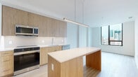 Located on the 11th floor at 4909 Auburn Ave in Bethesda, MD, this 2-bedroom, 1-bathroom residence offers a thoughtfully designed layout with a clean, contemporary aesthetic throughout. Light wood-tone flooring flows consistently across the living areas and bedrooms, contributing to a bright and cohesive atmosphere.

The kitchen serves as a central highlight, featuring warm wood cabinetry extending to the ceiling, white quartz countertops, a tiled backsplash, and a full suite of stainless steel appliances including a refrigerator, range, microwave, and dishwasher. A substantial kitchen island with a pendant light above provides additional workspace and casual seating.

The primary bedroom is generously proportioned, with a large floor-to-ceiling window framing impressive city skyline views — a standout feature of this high-floor unit. The second bedroom offers a clean, versatile space with light-filled interiors and warm flooring. Four closets throughout the unit provide ample storage.

The bathroom is finished with large-format light tile flooring, marble-tiled walls in the glass-enclosed shower, and polished gold hardware accents, lending a refined and upscale feel. Hallways connect the rooms efficiently, and the overall layout maximizes usable space. The unit presents a modern, move-in-ready environment well-suited for urban living in the heart of Bethesda.
