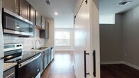 Located at 900 Owl Wood Ln in Summerville, SC, this single-floor residence showcases a thoughtfully designed open layout with modern finishes throughout. Rich hardwood flooring flows seamlessly across the living areas, complementing the neutral wall tones and crisp white trim that give the space a clean, contemporary feel.

The kitchen is a functional highlight, outfitted with gray shaker-style cabinetry, granite countertops, a classic white subway tile backsplash, and stainless steel appliances including a dishwasher, range, and microwave. A single-basin undermount sink adds a polished touch. A striking barn door with matte black hardware serves as a stylish divider, adding architectural character to the space.

The hallway connects key areas efficiently, revealing an in-unit stacked washer and dryer closet for added convenience. The main living area is bright and open, featuring a pair of large windows fitted with horizontal blinds that frame pleasant outdoor views of the surrounding community and greenery, flooding the room with natural light.

The bathroom features granite countertops consistent with the kitchen's design language, paired with hardwood-style flooring and clean, neutral walls. Recessed lighting throughout the home ensures well-distributed illumination. The overall ambiance is modern, clean, and move-in ready, reflecting quality craftsmanship in a well-appointed Summerville community.