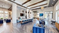 Located in Matthews, NC, this single-story community clubhouse offers a generously sized, open-concept layout designed for both relaxation and socializing. The main living area is anchored by soaring ceilings with exposed dark wood beam accents and large floor-to-ceiling windows that flood the space with abundant natural light and provide views of the surrounding greenery. Herringbone-patterned hardwood flooring runs throughout, complemented by a sophisticated blue and neutral color palette. Stylish pendant lighting, including a striking geometric diamond chandelier, enhances the contemporary aesthetic.

The social hub features a sleek bar counter lined with teal upholstered stools, set against a mosaic tile accent wall with wall-mounted media. An adjacent game room showcases a full-size billiards table beneath an eye-catching lattice wood ceiling fitted with Edison-style pendant lights, creating a warm, inviting atmosphere. A cozy lounge area with channel-tufted blue velvet seating surrounds a wall-mounted TV set into white brick, crowned by a dramatic ring chandelier. A dedicated workspace offers built-in desks, modern task seating, and stylish pendant lighting for productivity. The patio extends the living space outdoors, rounding out this well-appointed community retreat.
