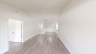 This single-floor unit offers a clean, modern aesthetic defined by crisp white walls, light-toned wood-style flooring, and an abundance of natural light throughout. The open-concept living and dining area is immediately welcoming, anchored by impressive vaulted ceilings that lend a sense of volume and airiness to the space. Large sliding glass doors lead out to a private balcony, framing views of mature surrounding trees and bringing the outdoors in.

The kitchen is thoughtfully appointed with bright white shaker-style cabinetry, recessed lighting, and gleaming stone-look countertops that extend into a peninsula — ideal for casual dining or meal prep. A stainless steel sink and full suite of appliances, including a refrigerator, electric range, and built-in microwave, complete the functional layout.

The bedroom areas continue the home's light and airy feel, with generous proportions, large windows offering garden views, and vaulted ceilings in the primary space. The bathroom is well-appointed, featuring a glass-enclosed shower, white vanity with stone countertop, and a large mirror. A dedicated in-unit laundry room with full-size washer and dryer, built-in shelving, and additional storage rounds out this well-designed and move-in-ready space.