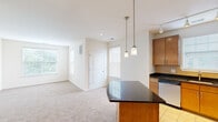 Located in Cherry Hill, NJ, this well-designed one-bedroom, one-bathroom unit offers a thoughtful single-floor layout that maximizes functionality and comfort. The open-concept kitchen and living area serves as the heart of the space, where warm wood cabinetry, dark granite countertops, and a central island create a polished and practical kitchen. Stainless steel appliances — including a refrigerator, range, microwave, and dishwasher — complement the design, while pendant lighting and track lighting illuminate both the kitchen and the adjoining living area. Light tile flooring in the kitchen transitions to soft wall-to-wall carpeting in the living room, adding warmth underfoot. Multiple windows throughout the unit allow natural light to fill each room, fostering a bright and airy ambiance. The bedroom offers a comfortable, carpeted retreat with windows overlooking greenery, providing a calm and private atmosphere. A closet door is visible, offering convenient storage. The bathroom features tile flooring and tiled shower walls in earthy tones, accented by clean, neutral finishes. Overall, the unit presents a clean, neutral palette throughout, making it a versatile and move-in ready living space.
