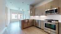This well-appointed 1-bedroom, 1-bathroom residence features a contemporary open-concept layout that seamlessly connects the kitchen and living areas. The kitchen is a standout, showcasing flat-front wood-grain cabinetry, a full suite of stainless steel appliances including a gas range, dishwasher, microwave, and refrigerator, as well as a subway tile backsplash, quartz countertops, and a peninsula with a deep stainless steel farmhouse sink. Pendant lighting and under-cabinet illumination add a refined touch, while light hardwood flooring extends throughout the main living area. The living space is bright and airy, benefiting from large windows and a ceiling fan. The bedroom offers plush carpeting, dual windows with neighborhood views, and a calm, neutral palette. The bathroom is elegantly finished with a chevron-patterned tile floor that blends wood and stone tones, large-format gray wall tiles in the tub/shower surround, a built-in niche, and a floating vanity with quartz countertop and wood-grain cabinetry. Clean lines, modern hardware, and a cohesive neutral color scheme unify the space, creating a polished and functional home.