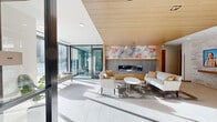 The Eloise is a thoughtfully designed single-floor amenity space spanning a generous footprint that accommodates a diverse range of communal functions. The welcoming lobby immediately sets the tone with soaring wood-paneled ceilings, large floor-to-ceiling glass walls that flood the space with natural light, and a sleek linear fireplace crowned by a vibrant large-scale artwork. Comfortable lounge seating and polished tile flooring create an inviting first impression. The living and lounge area continues the modern aesthetic with distinctive blue acoustic ceiling baffles, a built-in media wall, and soft neutral furnishings that invite relaxation. The kitchen features crisp white cabinetry, a striking deep-blue hexagonal tile backsplash, quartz countertops, and stainless steel appliances. The adjacent dining area is bright and functional, with light wood tones, teal upholstered seating, and curated artwork along the walls. A dedicated golf simulator room offers a turf putting surface, projection screen, and bar-height seating for an engaging recreational experience. The fitness center is well-appointed with a full array of cardio and strength equipment, patterned carpeting, and large windows overlooking the outdoors. A charming hallway vignette features tiered floating shelves lined with lush greenery, adding a natural, lively touch throughout the space.