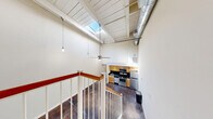 Located at 3031 Norfolk St in Richmond, VA, this 1-bedroom, 1-bathroom loft-style unit offers a striking industrial-modern aesthetic with a thoughtful layout. The main living level showcases polished concrete floors throughout, soaring double-height ceilings, and an abundance of vertical space that lends an airy, open atmosphere. A dramatic skylight overhead floods the interior with natural light, while exposed ductwork and pendant lighting add to the unit's contemporary industrial character. The open-concept main level seamlessly combines the living room, dining area, and kitchen. The kitchen is equipped with stainless steel appliances — including a gas range, dishwasher, and refrigerator — complemented by warm honey-toned cabinetry and dark countertops. Exposed brick accents along the walls further enhance the loft's character. A white-painted wood staircase with a warm wood handrail leads to the upper level, where the carpeted bedroom provides a comfortable retreat, complete with a ceiling fan. The bedroom level also provides convenient access to the in-unit laundry. Two closets offer practical storage throughout the unit. The overall ambiance is a seamless blend of industrial character and residential warmth, making this a distinctive space in Richmond's Norfolk Street corridor.