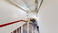 Located at 3031 Norfolk St in Richmond, VA, this 1-bedroom, 1-bathroom loft-style unit offers a striking industrial-modern aesthetic with a thoughtful layout. The main living level showcases polished concrete floors throughout, soaring double-height ceilings, and an abundance of vertical space that lends an airy, open atmosphere. A dramatic skylight overhead floods the interior with natural light, while exposed ductwork and pendant lighting add to the unit's contemporary industrial character. The open-concept main level seamlessly combines the living room, dining area, and kitchen. The kitchen is equipped with stainless steel appliances — including a gas range, dishwasher, and refrigerator — complemented by warm honey-toned cabinetry and dark countertops. Exposed brick accents along the walls further enhance the loft's character. A white-painted wood staircase with a warm wood handrail leads to the upper level, where the carpeted bedroom provides a comfortable retreat, complete with a ceiling fan. The bedroom level also provides convenient access to the in-unit laundry. Two closets offer practical storage throughout the unit. The overall ambiance is a seamless blend of industrial character and residential warmth, making this a distinctive space in Richmond's Norfolk Street corridor.