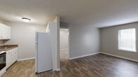 Located at 116 Brock St in Carrollton, GA, this single-floor, one-bedroom, one-bathroom unit offers a practical and efficiently arranged layout. The open kitchen and living area share a connected footprint, with wood-look plank flooring running throughout. The kitchen is equipped with white cabinetry, a dark laminate countertop, an electric range with overhead ventilation, a single-basin sink, and a full-size refrigerator. A partial wall divides the kitchen from the living area, which provides a clean, open feel with neutral gray walls and a textured ceiling. The living room also features a wall-mounted air conditioning unit and a door providing exterior access. The bedroom offers comfortable proportions, soft carpet flooring, a window with blinds allowing natural light, a closet, and a textured ceiling. The bathroom is fitted with a white vanity with storage, a toilet, and a tub/shower combination with a curtain rod, all finished with wood-look tile flooring. Throughout the unit, clean white trim, neutral tones, and consistent flooring choices create a cohesive and functional living environment.