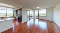 This well-appointed single-floor residence combines modern design with functional living. The open-concept main area is anchored by rich, warm-toned hardwood flooring that flows throughout the living and kitchen spaces, creating a cohesive and inviting atmosphere. Floor-to-ceiling windows and sliding glass doors bathe the living room in natural light while offering sweeping elevated views of the surrounding cityscape and lush greenery beyond.

The kitchen is thoughtfully designed with dark wood cabinetry, granite countertops, a decorative tile backsplash, and a full suite of stainless steel appliances, including a French door refrigerator and dishwasher. A peninsula provides additional counter space and connects seamlessly to the main living area.

The bedrooms are carpeted for comfort, each benefiting from large windows that frame outdoor views and allow generous natural light. One bedroom features a walk-in closet, providing ample storage. The two full bathrooms are finished in a clean, contemporary style with large-format tile flooring, white vanities with modern hardware, and full soaking tub and shower combinations. The overall ambiance throughout the residence is bright, neutral, and move-in ready, offering a polished urban living experience.