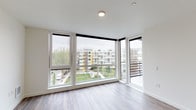 Located on the fifth floor at 2100 East Madison Street in Seattle's Capitol Hill neighborhood, Unit 507 presents a thoughtfully designed single-level residence with a clean, contemporary aesthetic throughout. Wide-plank wood-style flooring extends across the open-concept living and kitchen area, creating a cohesive and warm visual continuity.

The kitchen is a standout feature, equipped with stainless steel appliances including a refrigerator, range, microwave, and dishwasher. Two-tone cabinetry pairs gloss white upper cabinets with wood-grain lower cabinets, complemented by a tile backsplash and light quartz countertops. Recessed lighting illuminates the workspace effectively.

The living area benefits from expansive floor-to-ceiling windows and a glass door that opens to a private balcony, flooding the interior with natural light and offering views of the surrounding Capitol Hill streetscape and greenery. The bedroom features wood-style flooring and window access to the balcony.

The bathroom is finished in a crisp, minimalist style with a soaking tub and shower combination, a wood-grain vanity with a white countertop, a large mirror, and coordinating fixtures. An in-unit stacked washer and dryer is also included, adding everyday convenience to this well-appointed residence.
