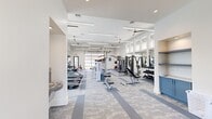Located at 111 Patterson Ln in Meridianville, Alabama, this modern fitness center offers a spacious, single-floor layout designed to support a comprehensive workout experience. The facility is characterized by soaring ceilings lined with sleek linear LED lighting and multiple ceiling fans that keep the space comfortable and well-ventilated throughout.

The main workout area is thoughtfully organized into distinct zones. A cardio section features a row of Spirit treadmills and cycling bikes positioned in front of expansive floor-to-ceiling windows that flood the space with natural light and frame views of an outdoor pool area. A dedicated strength training zone includes Body-Solid cable machines, weight benches, a full dumbbell rack, and plate-loaded equipment, all arranged around large wall mirrors that enhance the sense of openness.

A glass panel garage door opens to the outdoors, seamlessly connecting the interior to the surrounding grounds and providing additional ventilation and light. The flooring throughout the main area consists of durable, patterned carpet tiles in muted blue and grey tones. Built-in blue cabinetry and shelving near the restroom area provide convenient storage.

The facility also includes an ADA-accessible restroom finished with herringbone tile walls, dark floor tiles, and a wall-mounted sink — reflecting the same clean, modern aesthetic found throughout the space.