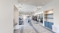 Located at 111 Patterson Ln in Meridianville, Alabama, this modern fitness center offers a spacious, single-floor layout designed to support a comprehensive workout experience. The facility is characterized by soaring ceilings lined with sleek linear LED lighting and multiple ceiling fans that keep the space comfortable and well-ventilated throughout.

The main workout area is thoughtfully organized into distinct zones. A cardio section features a row of Spirit treadmills and cycling bikes positioned in front of expansive floor-to-ceiling windows that flood the space with natural light and frame views of an outdoor pool area. A dedicated strength training zone includes Body-Solid cable machines, weight benches, a full dumbbell rack, and plate-loaded equipment, all arranged around large wall mirrors that enhance the sense of openness.

A glass panel garage door opens to the outdoors, seamlessly connecting the interior to the surrounding grounds and providing additional ventilation and light. The flooring throughout the main area consists of durable, patterned carpet tiles in muted blue and grey tones. Built-in blue cabinetry and shelving near the restroom area provide convenient storage.

The facility also includes an ADA-accessible restroom finished with herringbone tile walls, dark floor tiles, and a wall-mounted sink — reflecting the same clean, modern aesthetic found throughout the space.