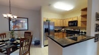 This single-floor residence offers a thoughtfully designed layout that balances comfort and functionality across its key living spaces. The kitchen is a standout feature, outfitted with warm honey-toned cabinetry, dark granite countertops, stainless steel appliances including a French door refrigerator and electric range, a built-in microwave, and a double sink. Light tile flooring runs throughout the kitchen, which also benefits from generous cabinet storage and open shelving. Adjacent to the kitchen, the dining area features elegant tile flooring, a pendant chandelier, and a bold dark accent wall that adds visual depth to the space. The living room is bright and welcoming, with light tile flooring, a sliding glass door that opens to a balcony with outdoor views, and neutral-toned walls complemented by rich drapery. The primary bedroom is carpeted and serene, featuring sliding glass door access to a private outdoor area, dual nightstands, and soft neutral tones. A second bedroom offers the same carpeted comfort with a cozy, restful ambiance. Two bathrooms are present — one with decorative patterned wallpaper, dark granite vanity, and a glass-door shower; the other with matching granite countertops, tile flooring, and a tub-shower combination. An in-unit laundry area completes this well-rounded residence.