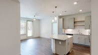 This single-floor residence is designed with a contemporary aesthetic and a functional open-concept layout. The kitchen serves as a central hub, featuring gray shaker-style cabinetry, granite countertops, a subway tile backsplash, and a full suite of stainless steel appliances including a refrigerator, range, microwave, and dishwasher. A central island with matching granite provides additional prep space and casual seating, while pendant lighting adds a refined touch overhead. Recessed lighting and hardwood-style flooring extend throughout the kitchen and into the adjoining living area, which benefits from natural light through sliding glass doors and large windows. The bedrooms are carpeted for comfort and each includes a ceiling fan and windows with outdoor views. A spacious walk-in closet offers multiple hanging rods and shelving for ample storage. The primary bathroom is finished with a dual-sink granite vanity, gray cabinetry with brushed nickel hardware, framed mirrors, and a tiled walk-in shower. The overall palette of soft whites, grays, and warm wood tones creates a clean, cohesive, and inviting atmosphere throughout the residence.