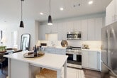 This contemporary 2-bedroom, 3-bathroom residence at 3300 Toledo Road in Hyattsville, MD offers a thoughtfully designed open-concept layout filled with natural light and modern finishes throughout. The kitchen is a standout feature, boasting sleek gray cabinetry extending to the ceiling, a white quartz waterfall island, stainless steel appliances, a subway tile backsplash, and striking black pendant lighting — all flowing seamlessly into the dining and living areas. The living room is bright and welcoming, with large windows dressed in floor-length drapes that invite abundant natural light and provide access to the private balcony. From the balcony, residents enjoy sweeping views of the building's courtyard pool and surrounding architecture. Both bedrooms are carpeted and serene, with the primary suite offering a spacious walk-in closet with built-in shelving and an en-suite bathroom featuring a glass-enclosed walk-in shower with clean white tile. The second bedroom is equally well-appointed with its own closet and bathroom access. Rich hardwood-style flooring anchors the main living areas, while clean white walls and recessed lighting lend a crisp, contemporary feel throughout this well-appointed Hyattsville residence.